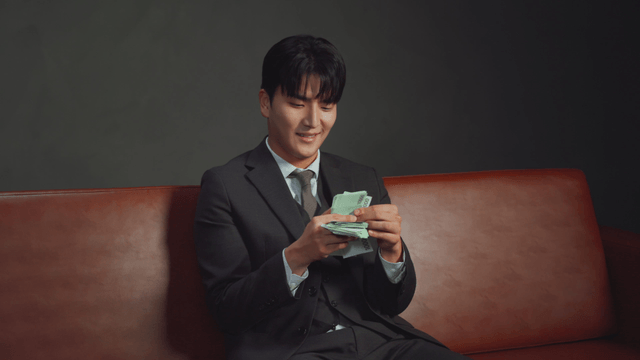 Man in a suit counting money on a sofa