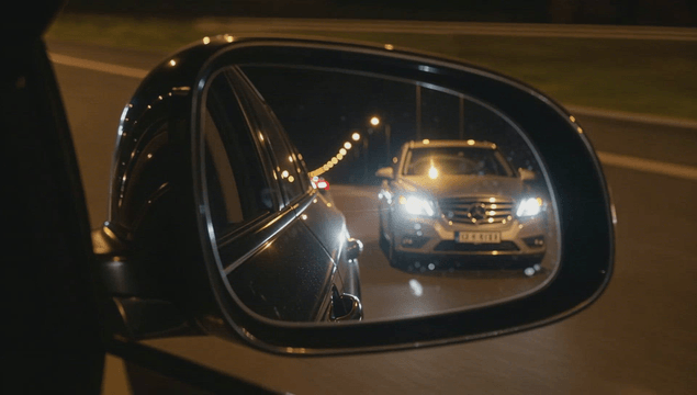 Car approaching closely at night seen through side mirror on the road