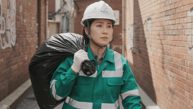 Female sanitation worker holding a trash bag in an alley