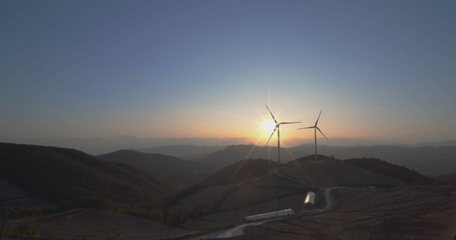 언덕 밭 위의 풍력 터빈 옆 눈부신 일출