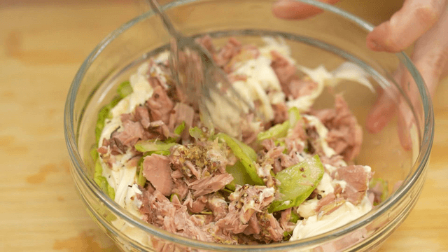 Fork mixing mayonnaise, cucumber, and tuna salad
