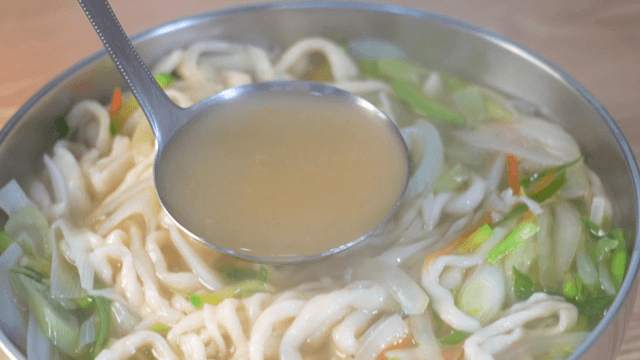 Ladle scooping rich broth of handmade noodle soup
