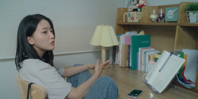 방에서 책상에 앉아 누군가와 대화하는 여성