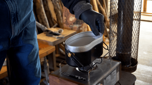 Person heating a mess tin with a portable burner indoors