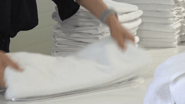 Workers folding many white towels in laundry factory