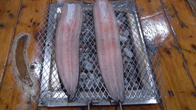 Eels being grilled on charcoal grate