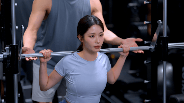 Young woman doing squats with a trainer's help