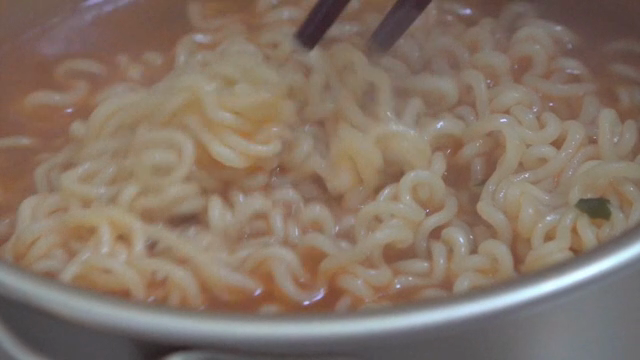 Chopsticks stirring ramyeon in a pot