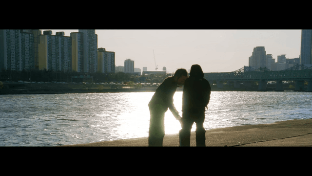 Two people practicing martial arts by the riverside with a city skyline background