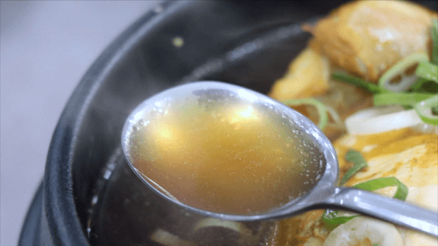 Spoon scooping clear broth from phellinus linteus ginseng chicken soup