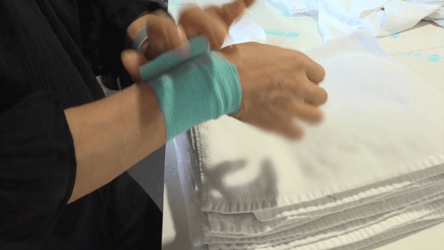 Worker with wrist guard folding white towels in factory