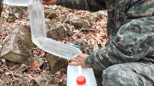Man in military uniform filling a water bottle with a plastic bag in the mountains