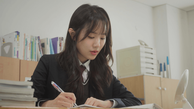 긴 웨이브 머리의 여학생이 교실에서 문제를 푸는 모습