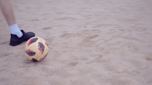 모래 운동장 위의 축구공에 슈팅을 차는 사람