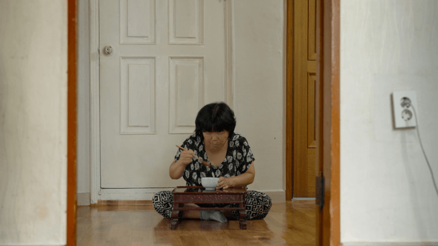 An elderly woman eating alone indoors