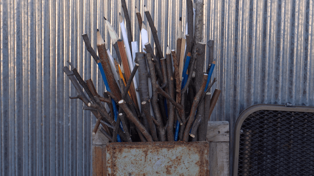 Wooden branch pencil sculpture against metal panel background