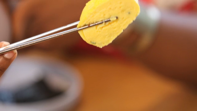 Chopsticks holding a piece of rolled omelette