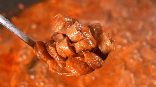 Ladle scooping sausage from boiling budaejjigae 