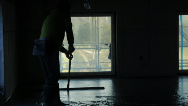 Worker smoothing concrete floor indoors