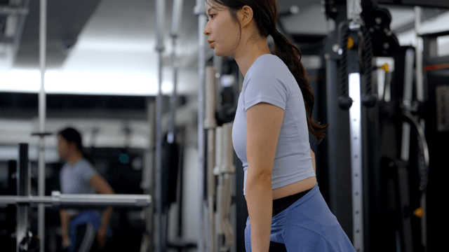 Side view of young woman doing lunges with dumbbells at gym