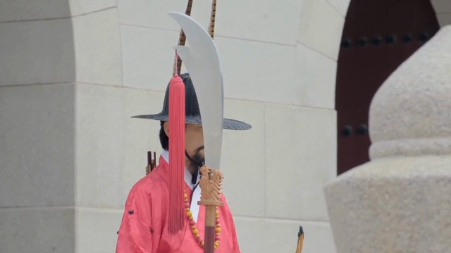 Traditional chief gatekeeper in red attire holding a weapon