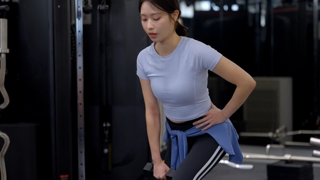 Young woman doing lunges with dumbbells at gym