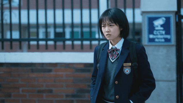 Short-haired schoolgirl leaving school gate with angry expression