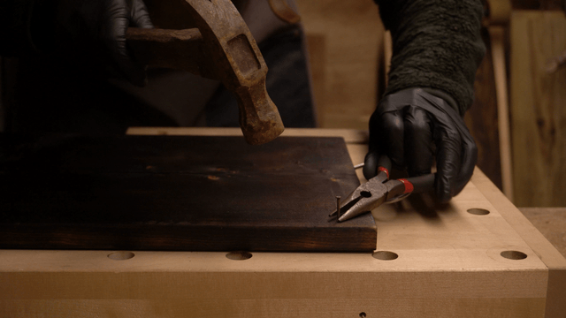 Black-clad artisan hammering a nail into a wooden board