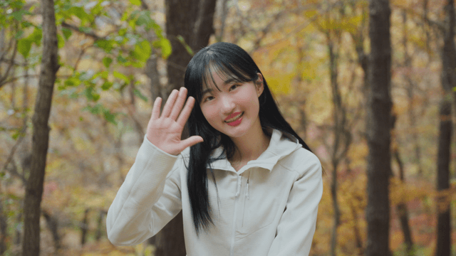 Smiling woman waving hand in autumn forest