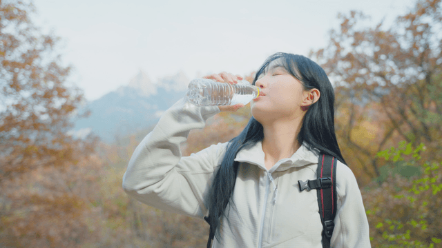 Woman drinking water on autumn trail with summit view