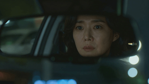 Rearview mirror reflecting a focused woman in the car at night