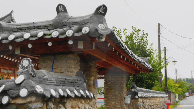 Rain falling over stone walls and eaves of a traditional hanok