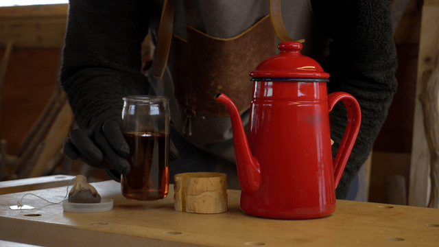 Red kettle and glass cup with tea and wooden sleeve