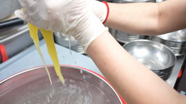 Gloved hands preparing yellow noodles