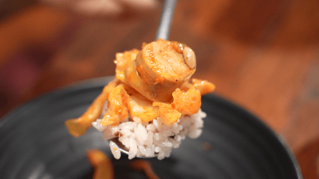 Sausage stir-fry placed on rice atop spoon