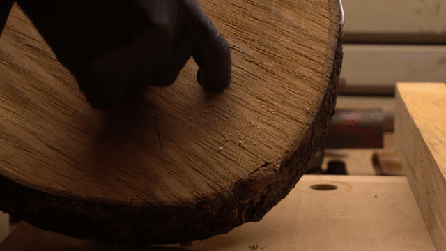 Gloved hands refining a hole in a wooden log