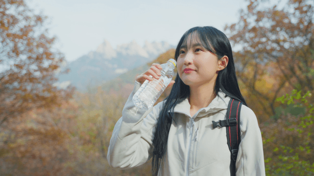Female hiker drinking water at autumn mountain summit