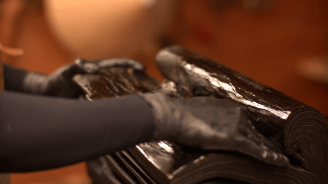 Artisan applying finishing oil to glossy wooden sculpture