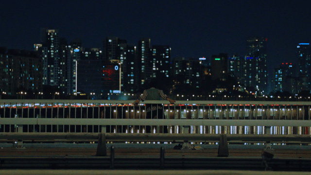 Man standing on a bridge railing with cars passing by