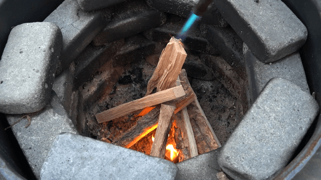Torch igniting neatly stacked firewood