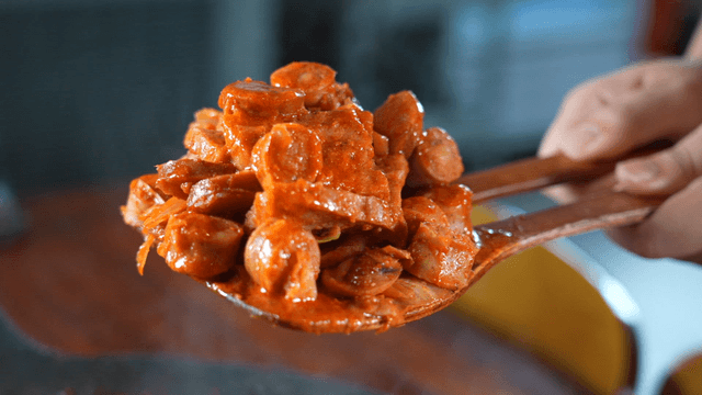 Wooden spatula lifting hot stir-fried sausage