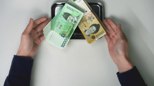 Hand offering a tray with Korean currency