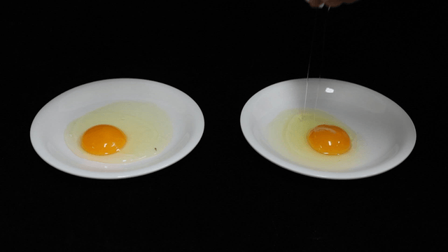 Two people cracking eggs onto white plate
