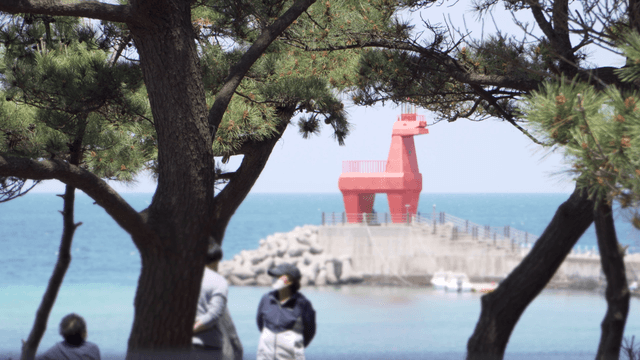Red horse-shaped lighthouse by the sea with trees