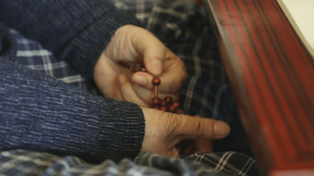 Old man holding prayer bead bracelet with cross on it