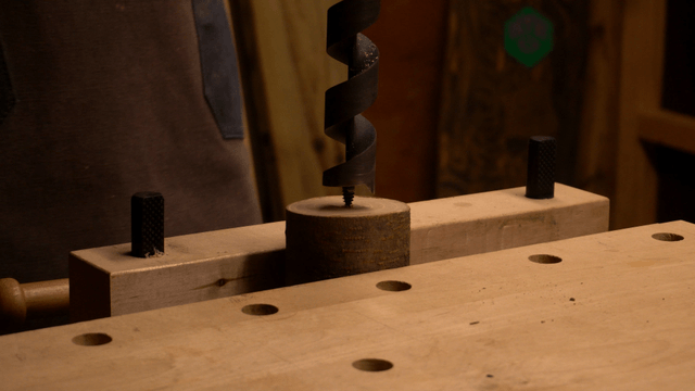 Artisan drilling wood piece with spiral bit on workbench