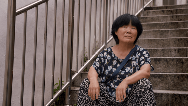 An elderly woman sitting on stairs looking at the sky