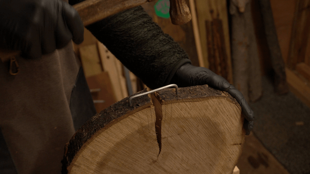 Craftsman hammering fixed wire into wooden log board