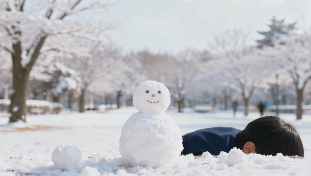 Happy boy building a snowman in a snowy park