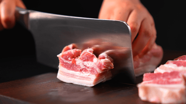 Slicing fresh pork belly on a wooden board